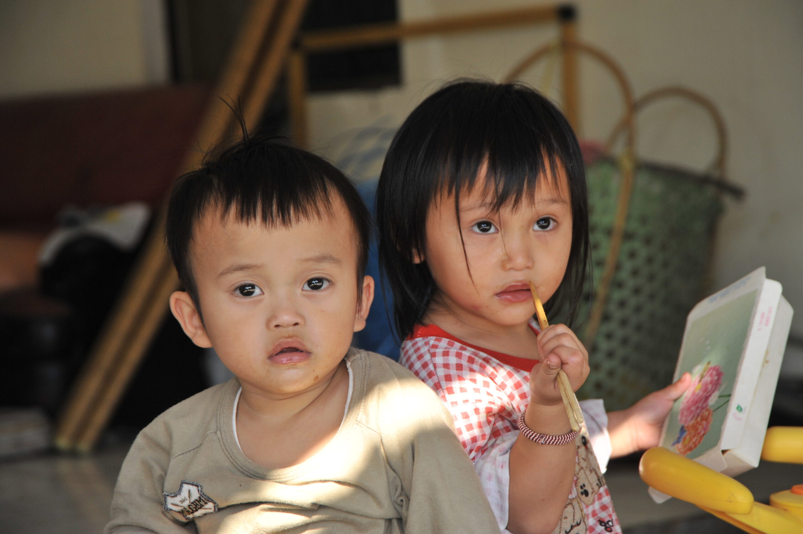Zwei taiwanische Kleinkinder, ein Junge und ein Mädchen, das Stäbchen an seinen Mund hält, schauen in die Kamera.