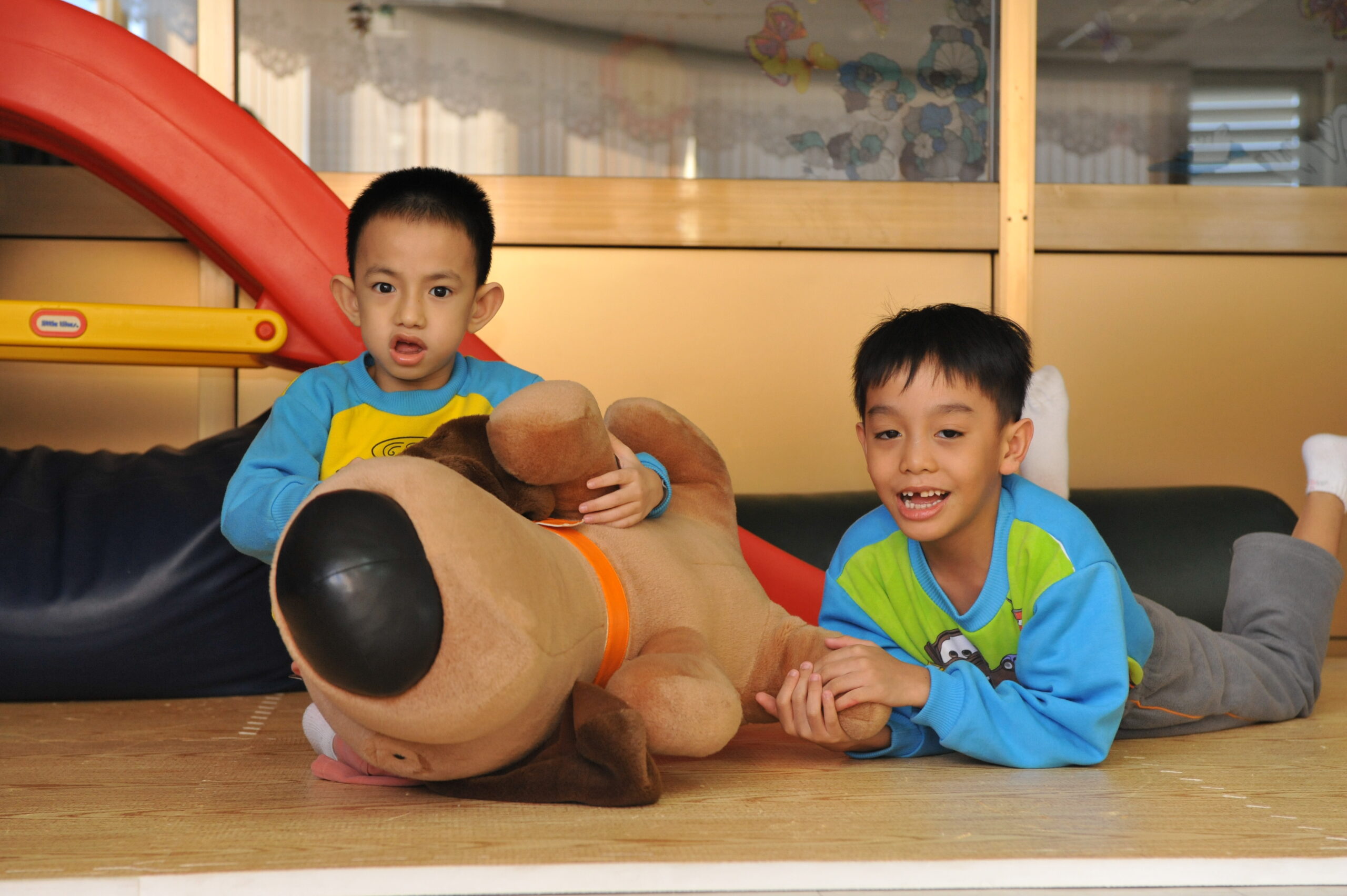 Zwei kleine taiwanische Jungen mit Behinderungen liegen neben einem Kuscheltierhund.