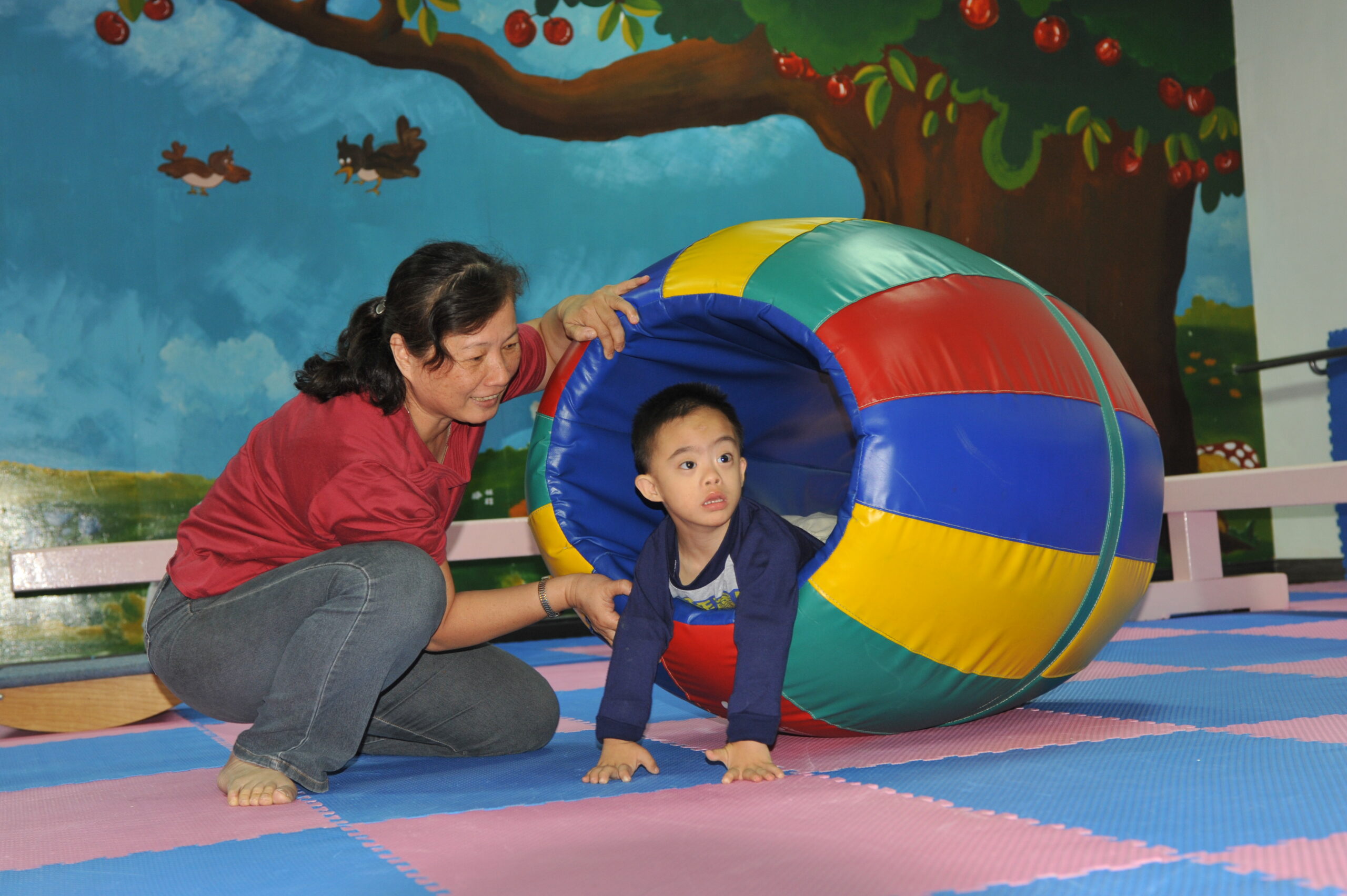 Eine Frau spielt mit einem kleinen Jungen mit Downsyndrom in einer Gymnastikröhre.