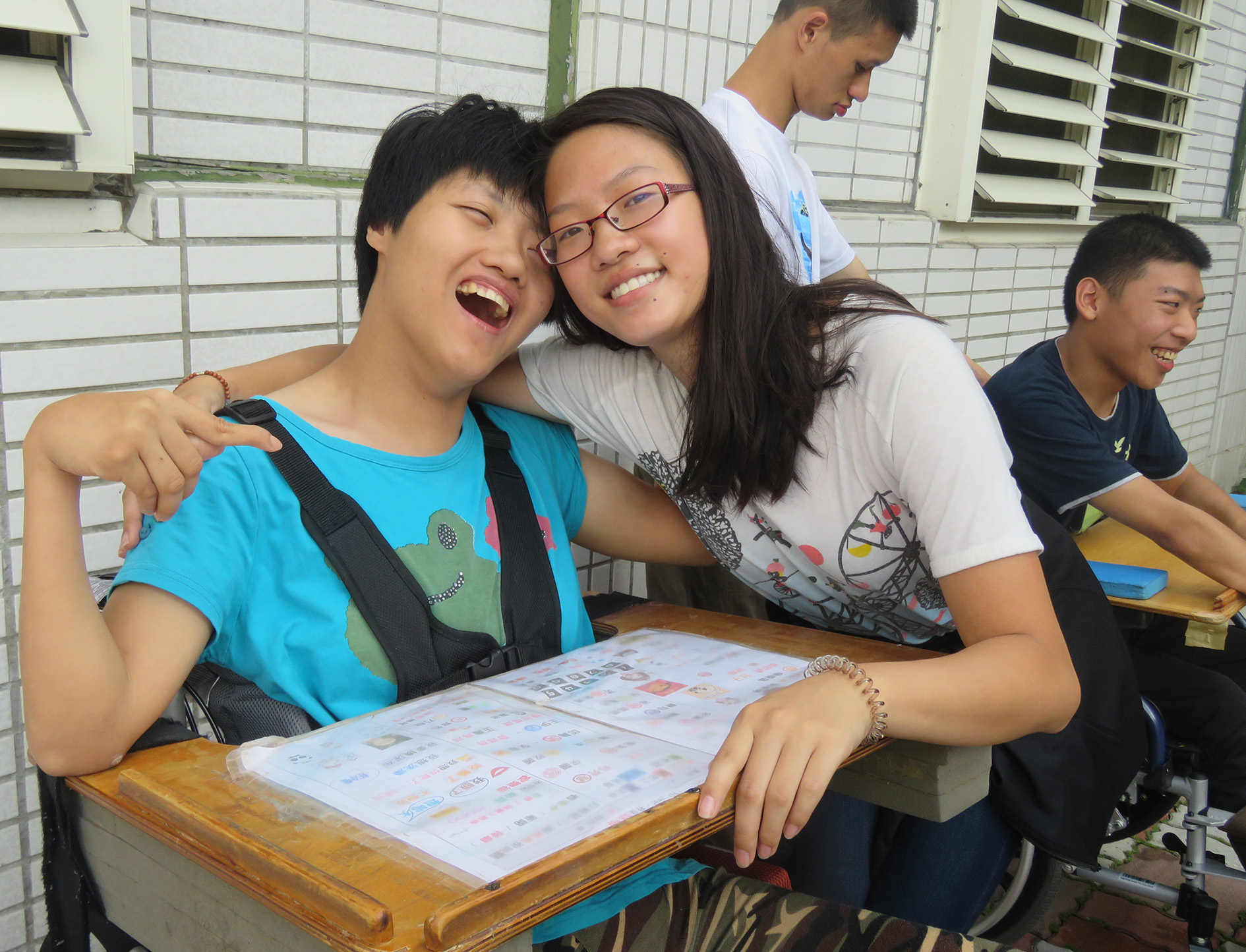 Eine amerikanische Frau und eine taiwanische Frau im Rollstuhl umarmen sich.